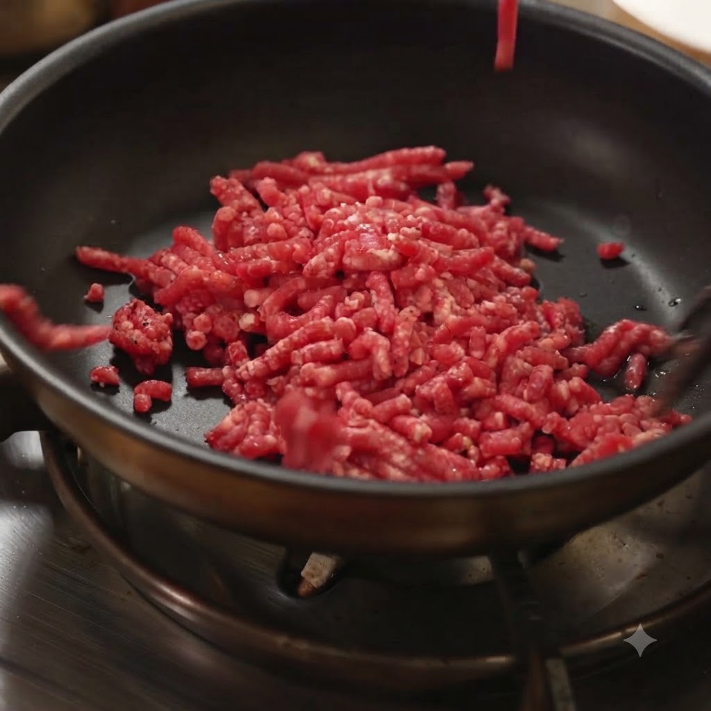 Carne macinata cruda che viene aggiunta in una padella nera calda su un piano cottura.