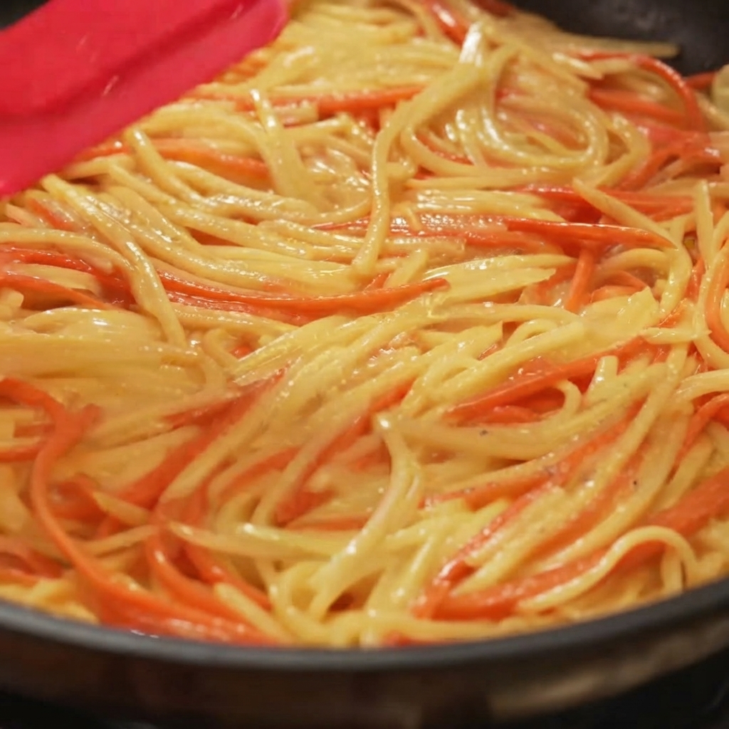 Una spatola che distribuisce e livella un composto di patate e carote in modo uniforme in una padella.