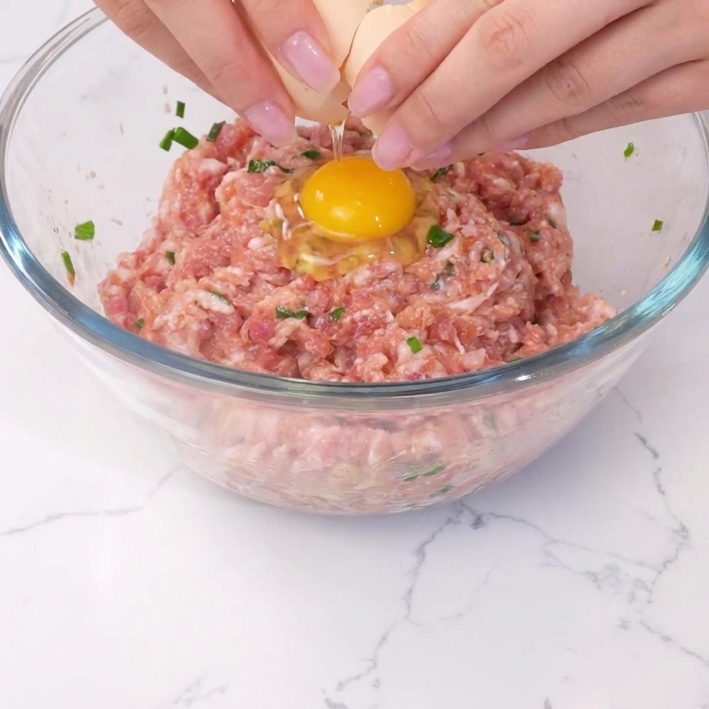 Un uovo che viene rotto al centro del composto di carne condito.
