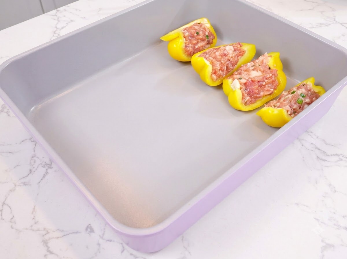Metà di peperone giallo ripiene di carne macinata condita disposte ordinatamente in una teglia viola.