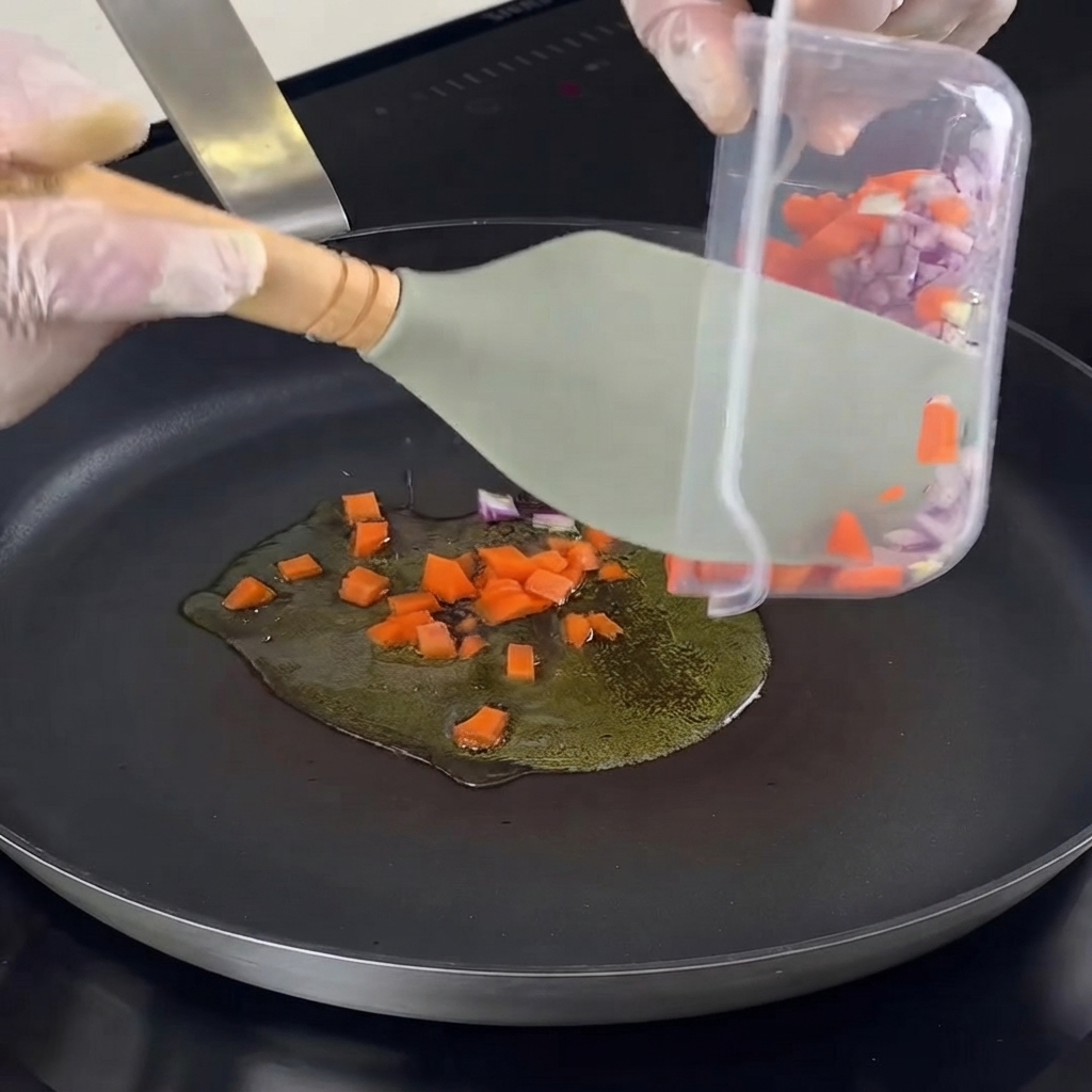 Cipolle, carote, aglio ed erbe tritati trasferiti in una padella calda con olio.