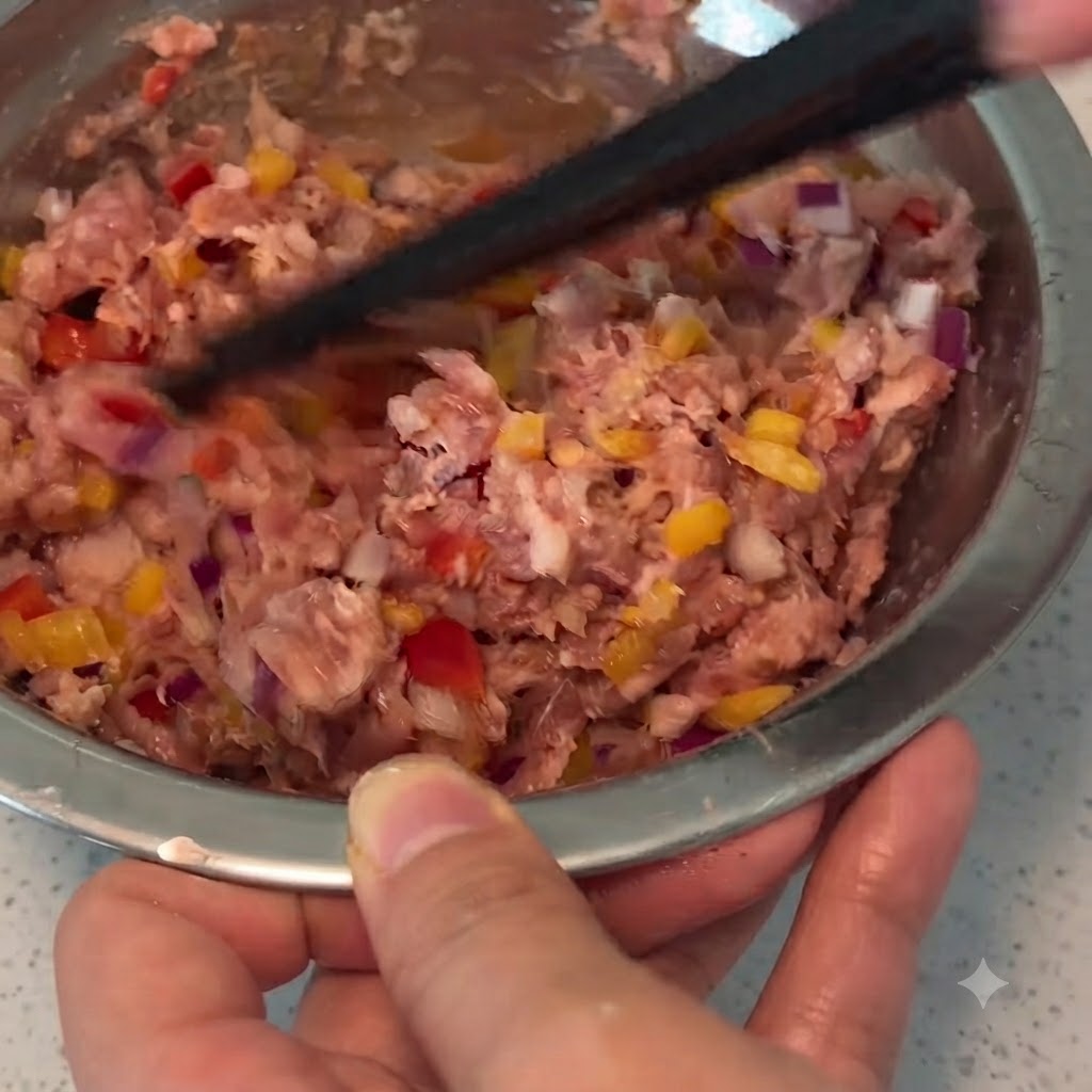 Un paio di bacchette che mescolano carne di maiale macinata, verdure e condimenti allinterno di una ciotola di metallo.
