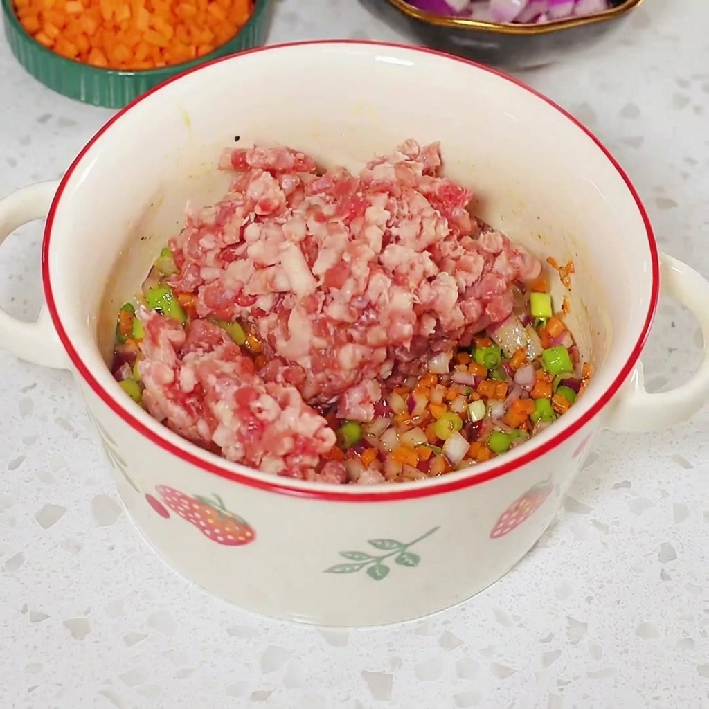 Carne macinata cruda posta sopra il composto di verdure condite allinterno di una ciotola bianca.