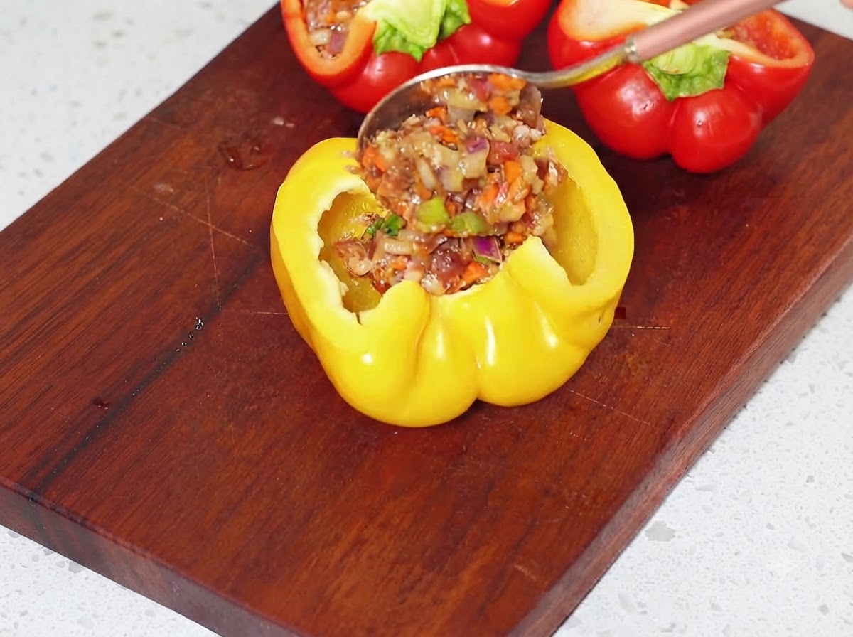 Riempire a cucchiaiate le metà svuotate di peperone giallo con il composto di carne preparato su un tagliere.