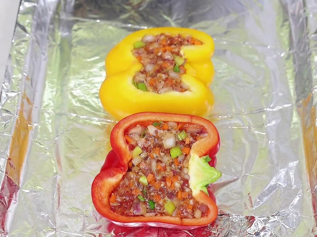 Metà di peperoni gialli e rossi ripieni riempiti con il composto di carne disposti su una teglia foderata di alluminio.