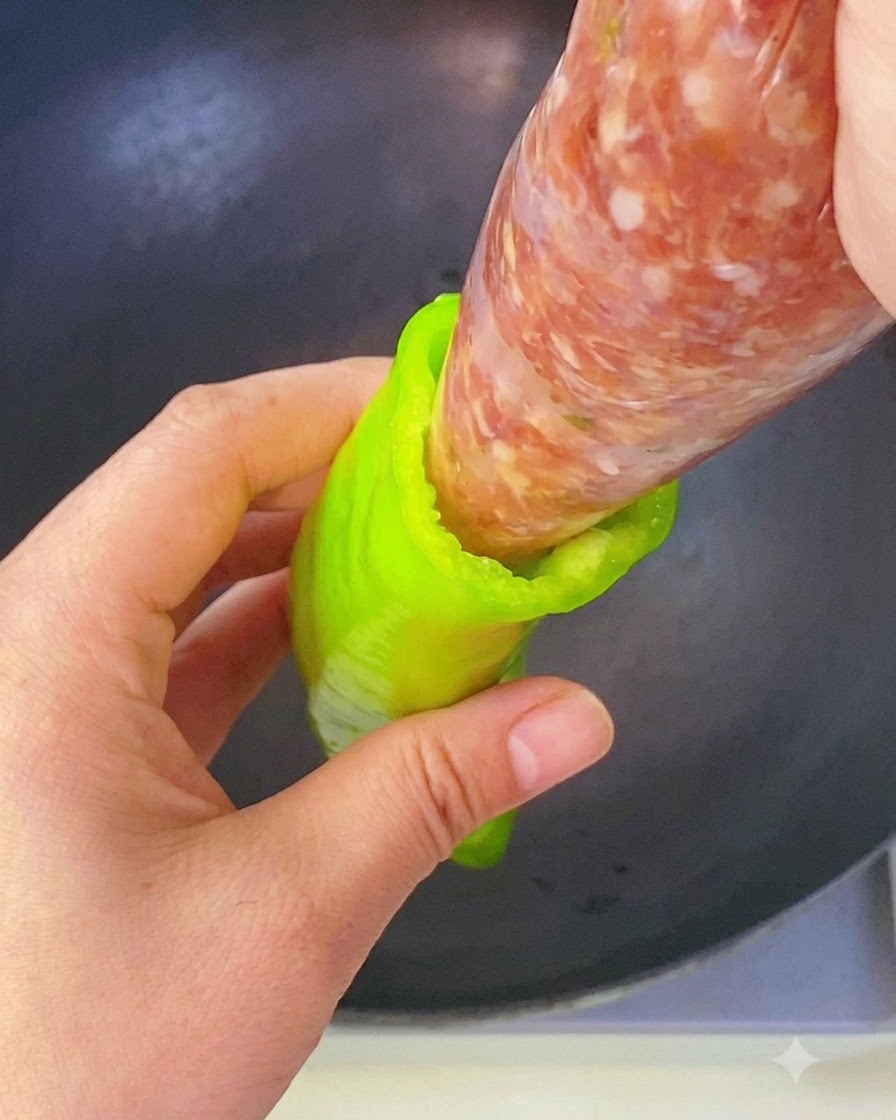 Una mano che spreme il ripieno di carne condita da una sacca da pasticcere direttamente nella cavità di un peperone verde.