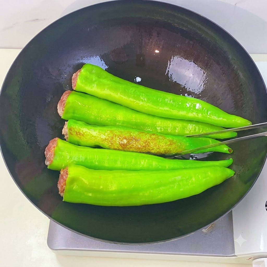 Peperoni verdi che friggono in un wok mostrando macchie marroni a pelle di tigre mentre vengono girati con le pinze da cucina.