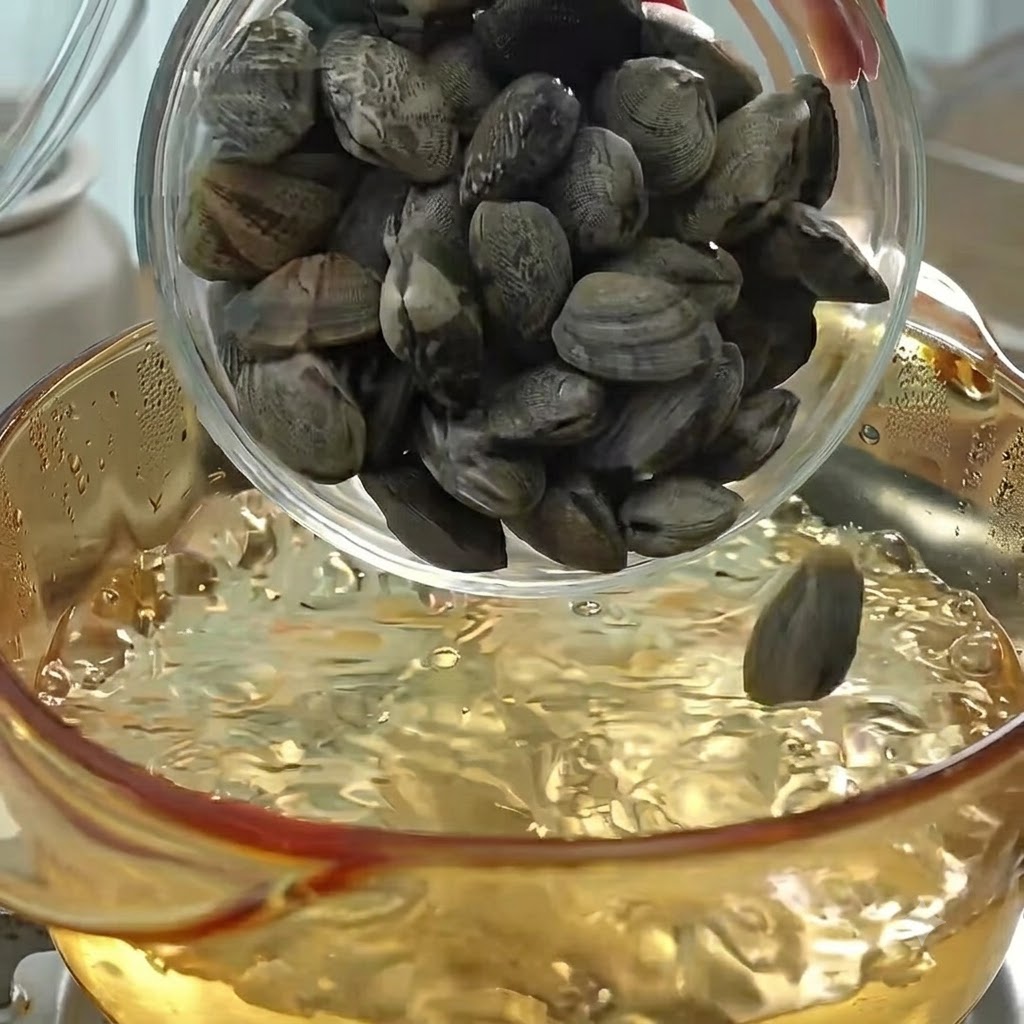 Vongole versate in una pentola di acqua bollente per cuocere e creare il brodo.