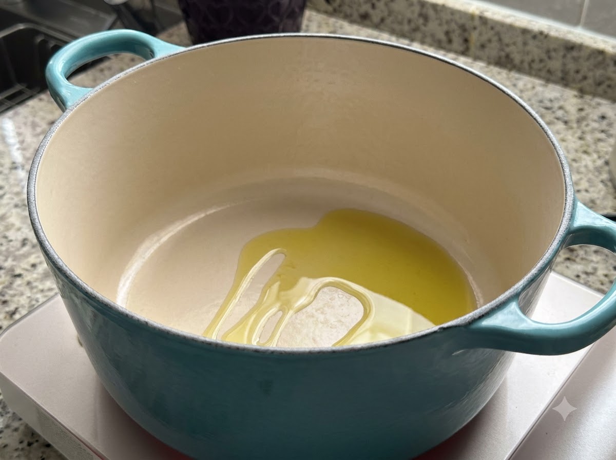 Una pentola olandese verde acqua su un piano cottura con una pozza di olio doliva che si scalda allinterno.