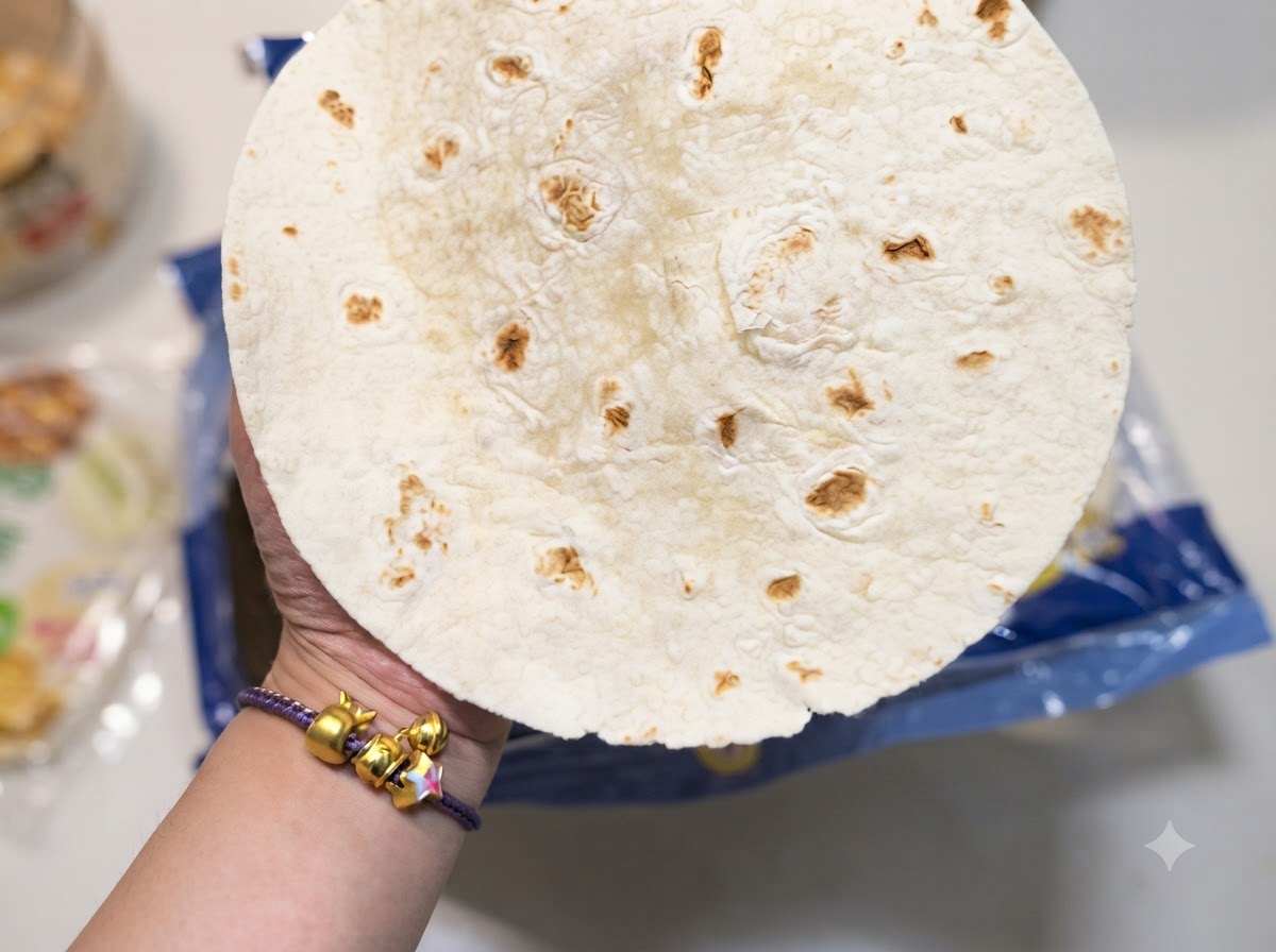 Una mano in primo piano che tiene una tortilla di farina rotonda con caratteristiche macchie marroni.