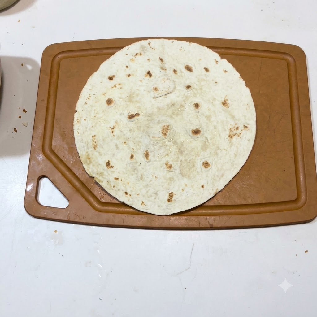Una singola tortilla calda distesa su una superficie di un tagliere marrone.