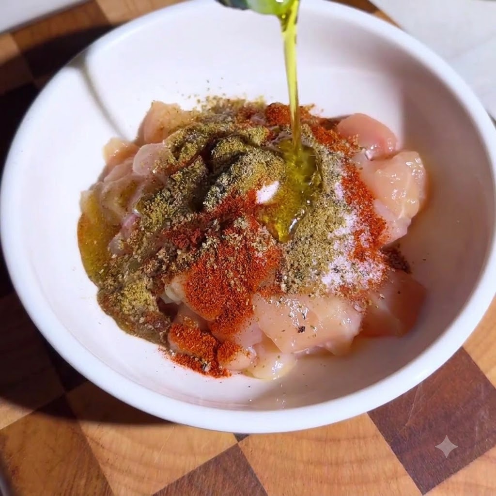 Una ciotola riempita di cubetti di pollo generosamente conditi con spezie miste e olio doliva.