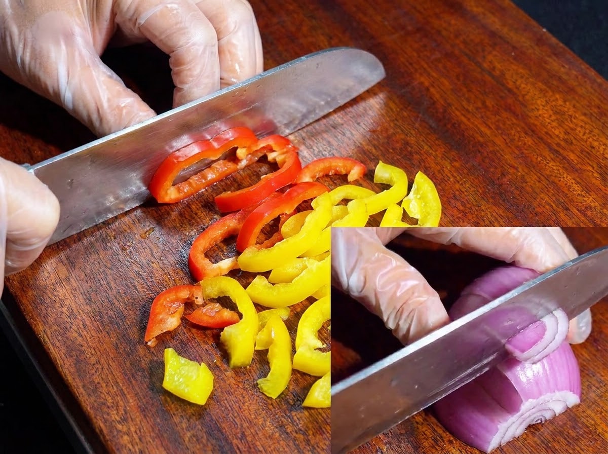Un coltello che taglia peperoni colorati e cipolla rossa su un tagliere di legno.