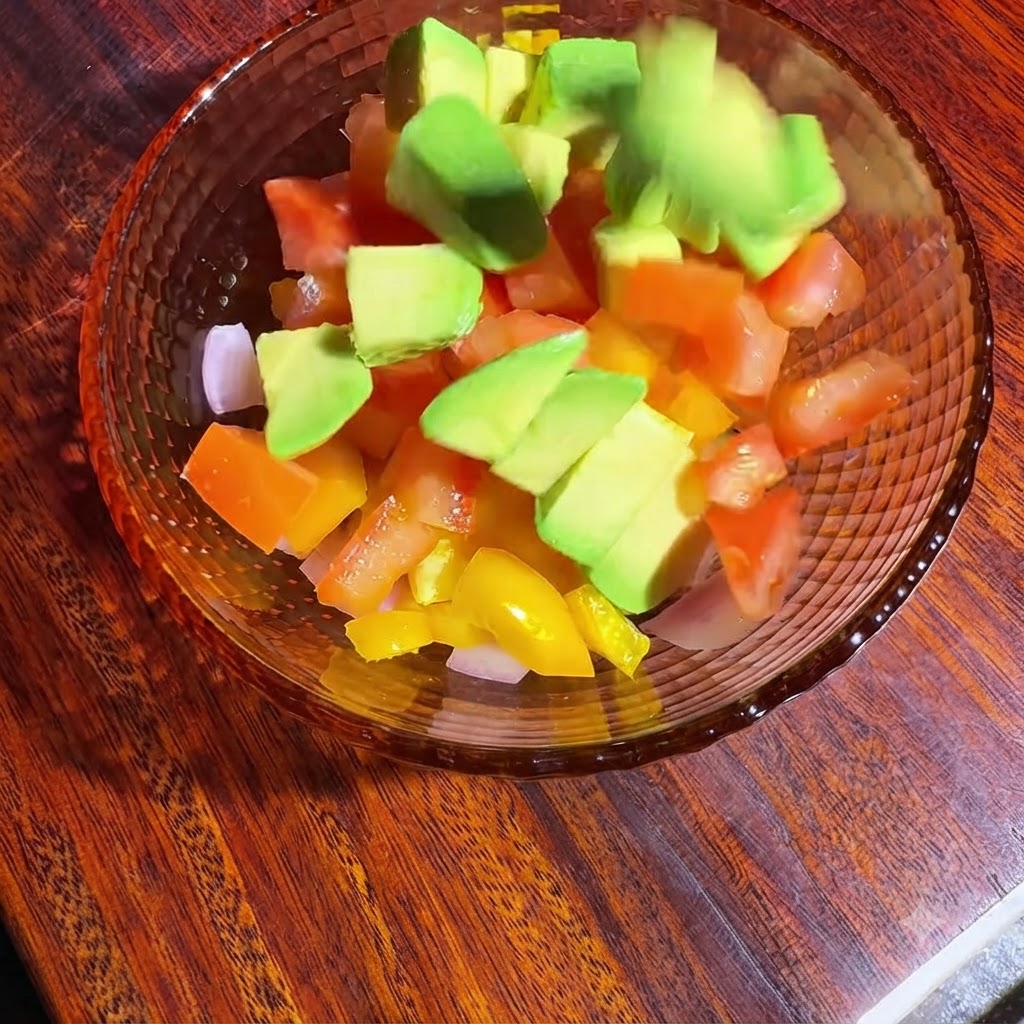 Una ciotola di verdure a cubetti e avocado mentre vengono mescolate e condite con olio e succo di limone.