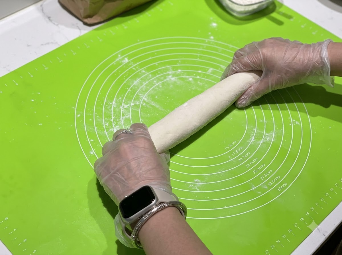 Mani che rotolano un salsicciotto di pasta su un tappetino in silicone verde con cerchi di misurazione.