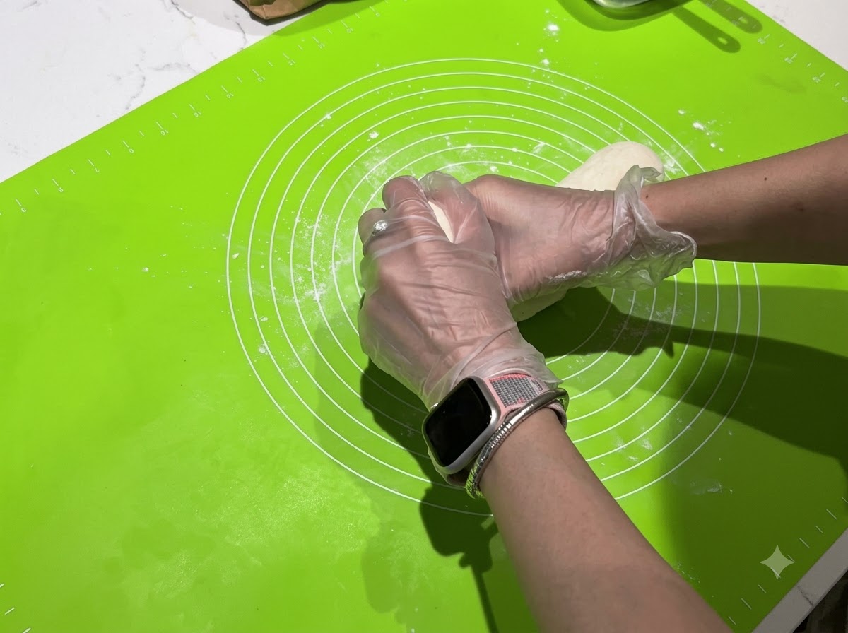 Mani che dividono una lunga striscia di impasto in pezzi singoli più piccoli su un tappetino verde.