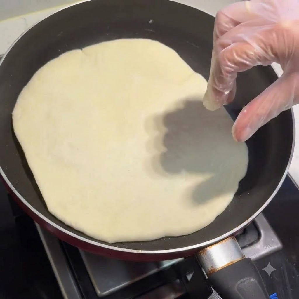 Una piadina che cuoce in una padella con una mano guantata che la sistema.