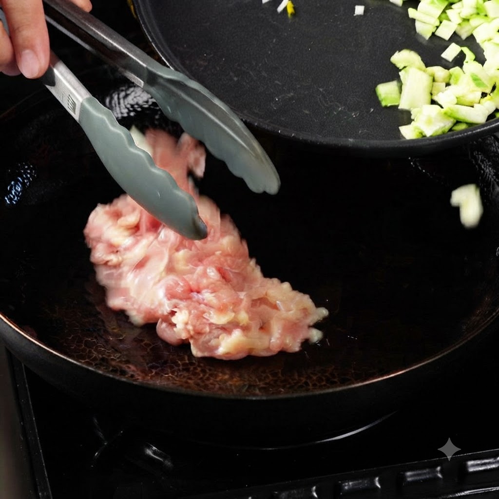 Dinamiche pinze che posizionano pezzi di pollo crudo in un wok riscaldato con olio, accanto a una padella contenente verdure tagliate a dadini.