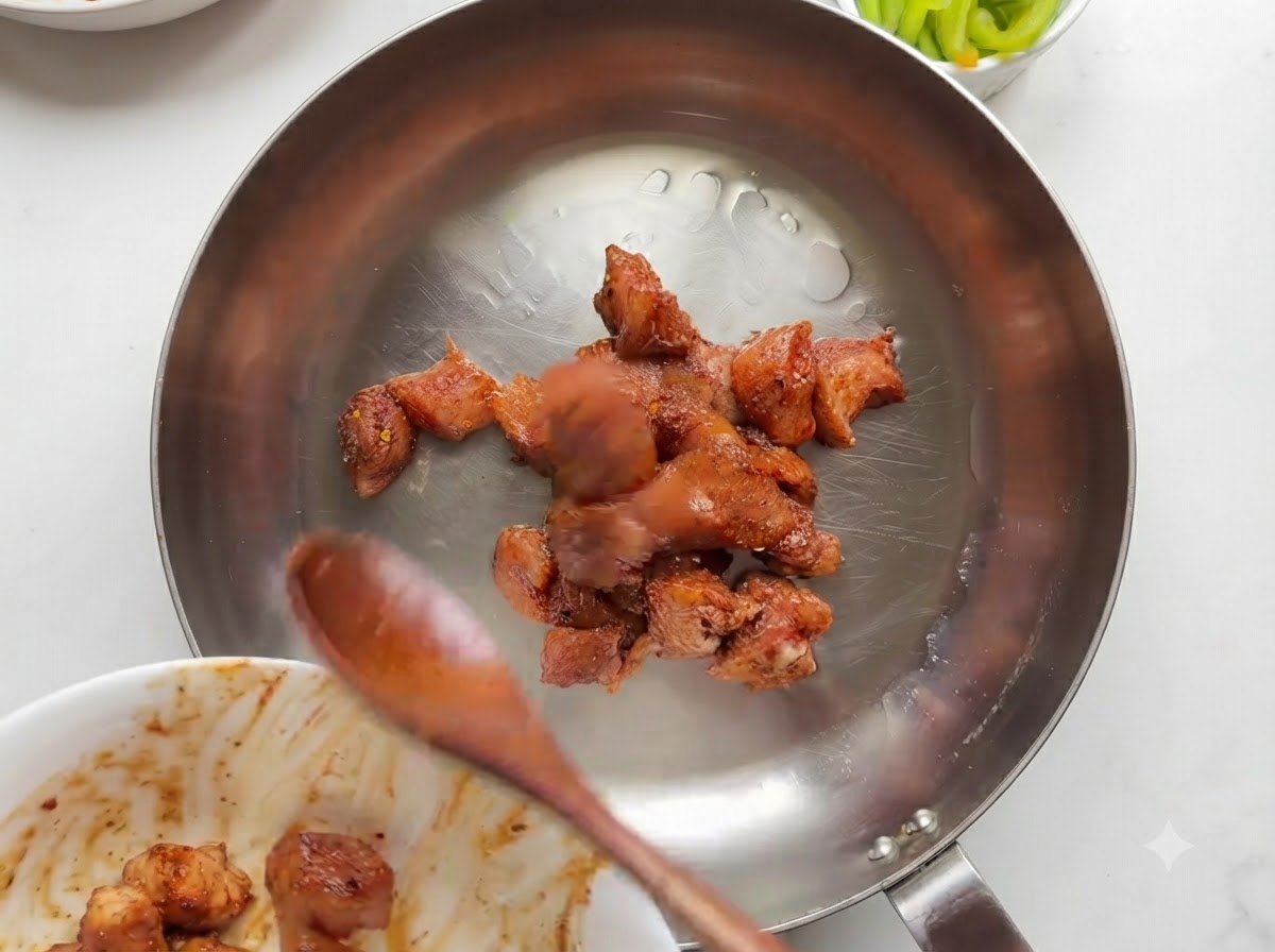 Pezzi di pollo marinati che cuociono e dorano in una padella in acciaio inossidabile.