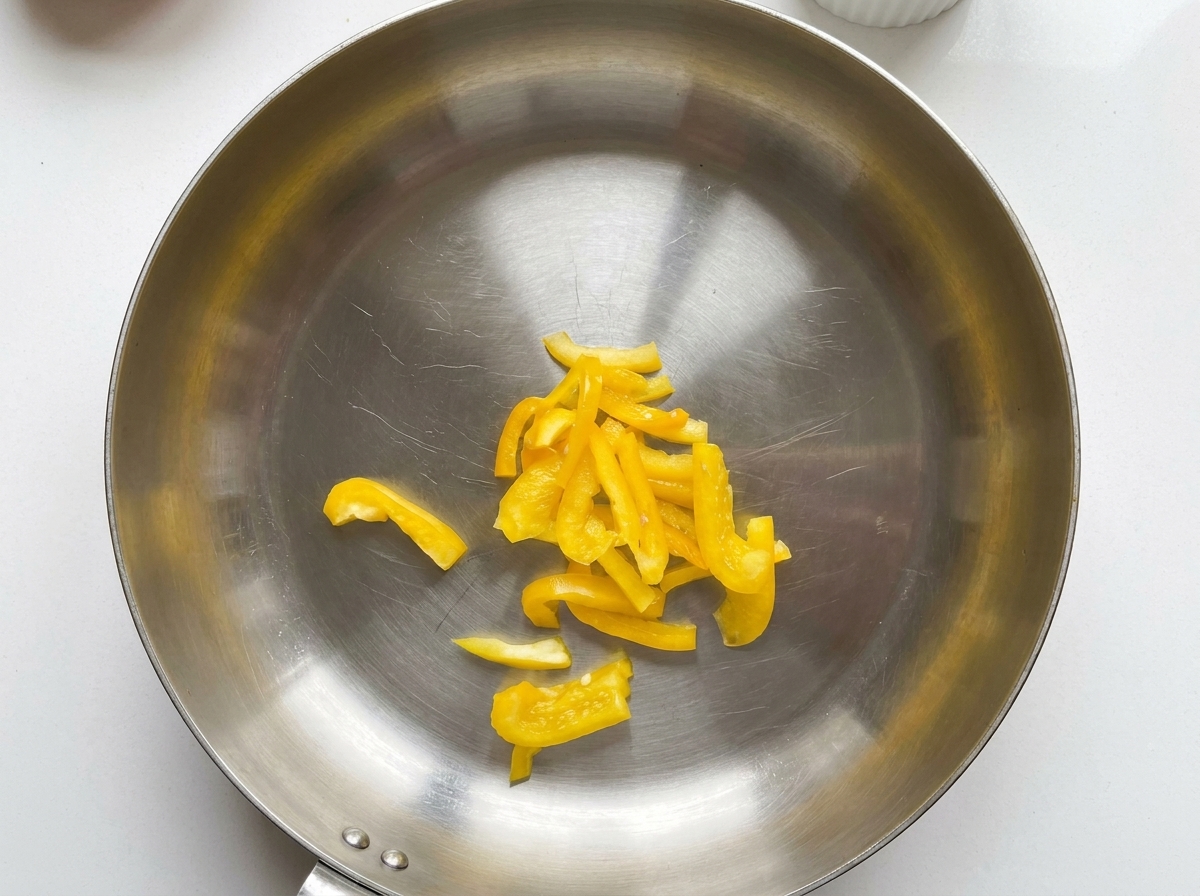 Peperoni gialli affettati posizionati al centro di una padella in acciaio inossidabile.