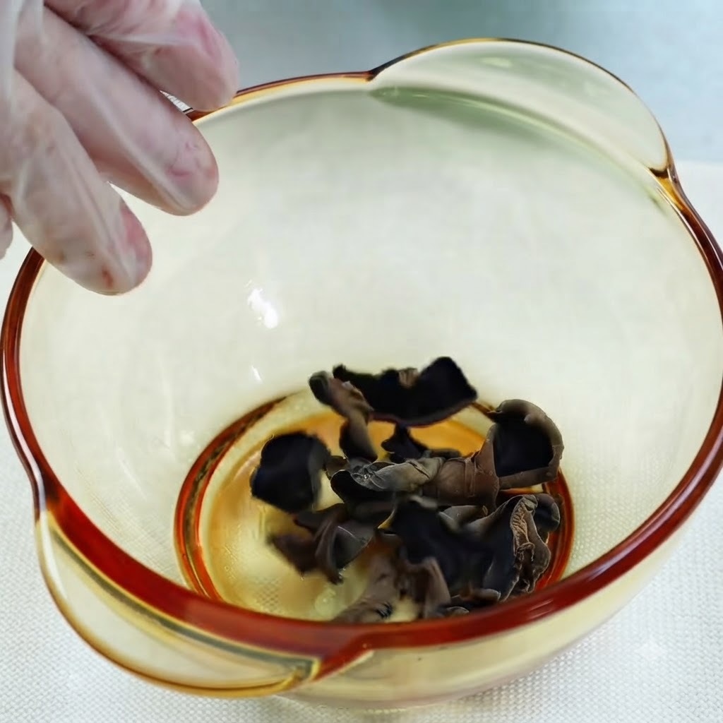 Acqua versata da un misurino di vetro in una ciotola di funghi orecchio di Giuda neri secchi.