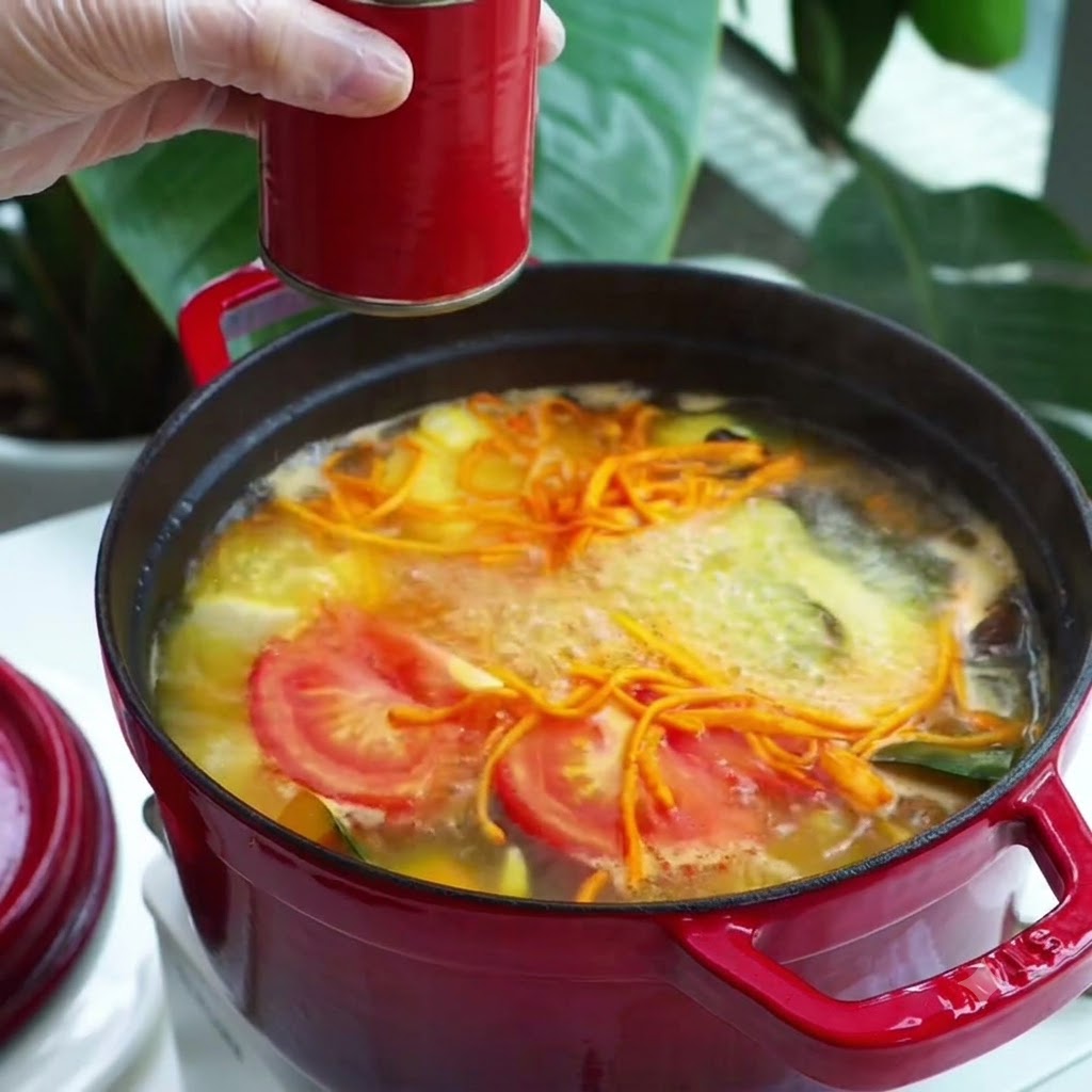 Un cucchiaio di condimento in pasta rossa aggiunto in una pentola di zuppa di verdure bollente.