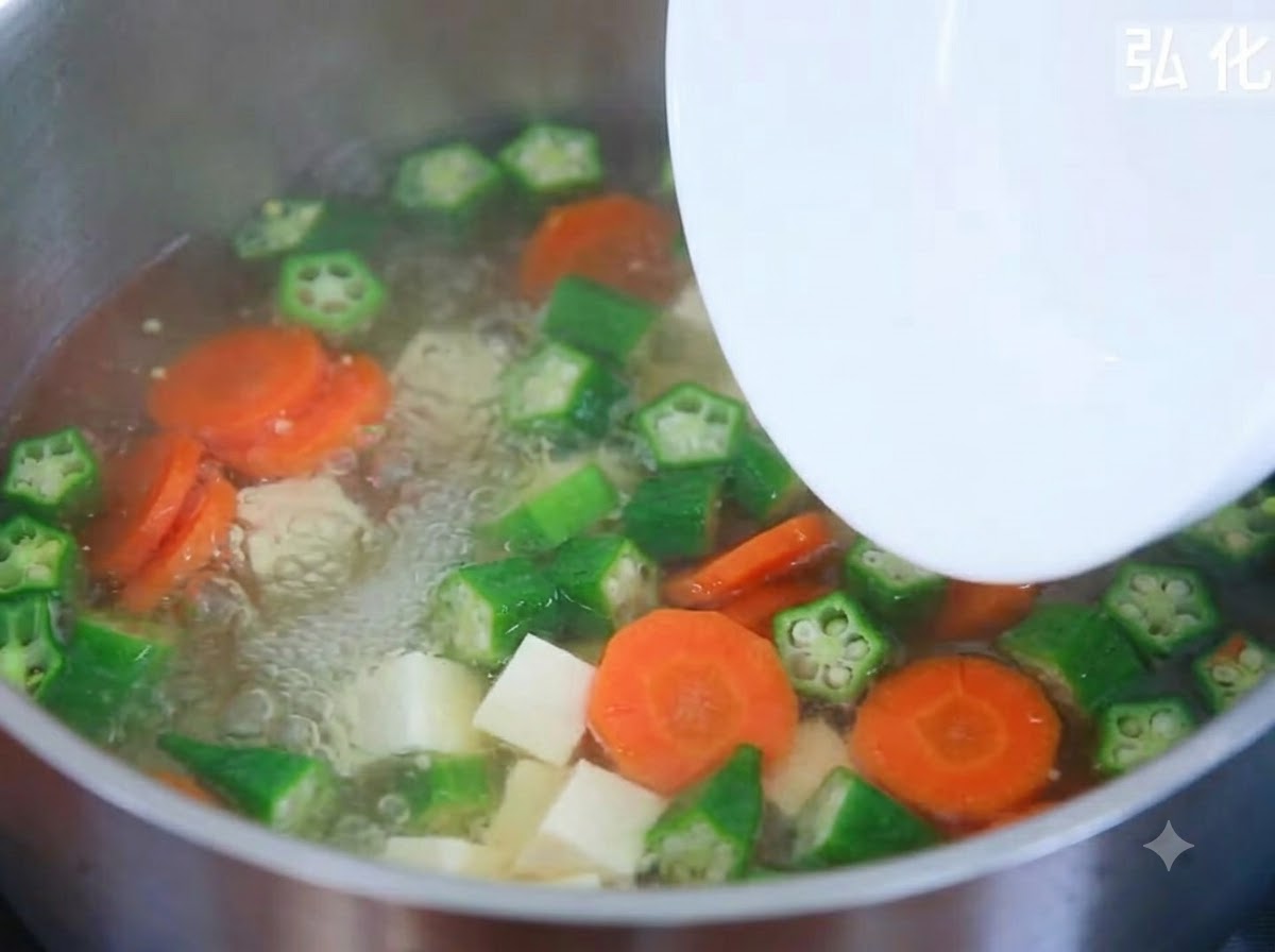 Cubetti di tofu morbido aggiunti da un piatto in una pentola ribollente di zuppa di verdure.