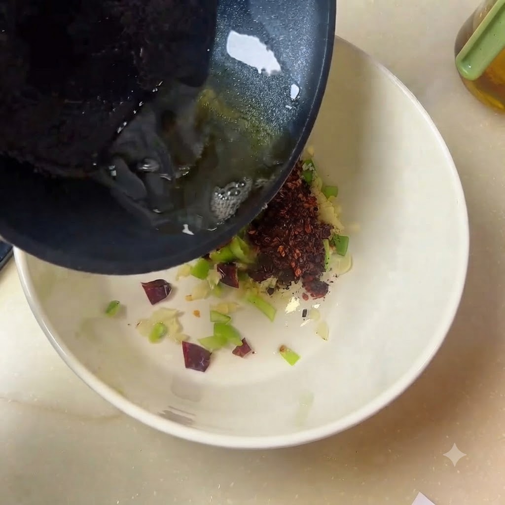Olio bollente che scorre da una padella in una ciotola bianca riempita di spezie e aromi.