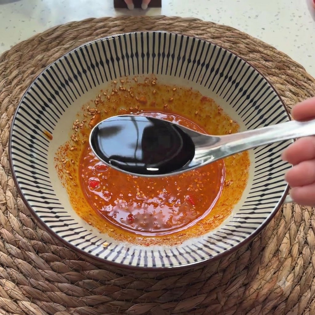 Salsa di soia chiara versata da un cucchiaio nella miscela di salsa condita.