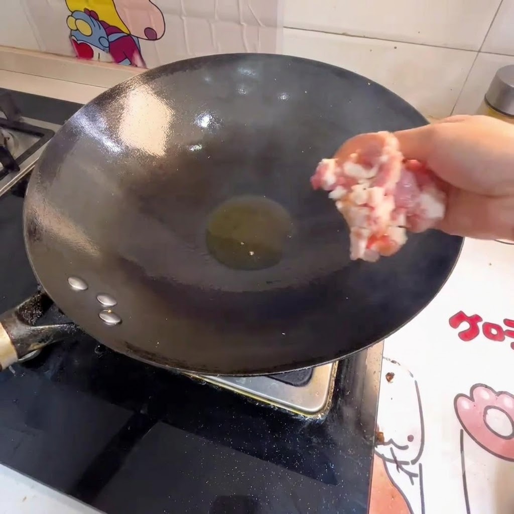 Mano che getta la carne macinata in un wok con olio caldo.
