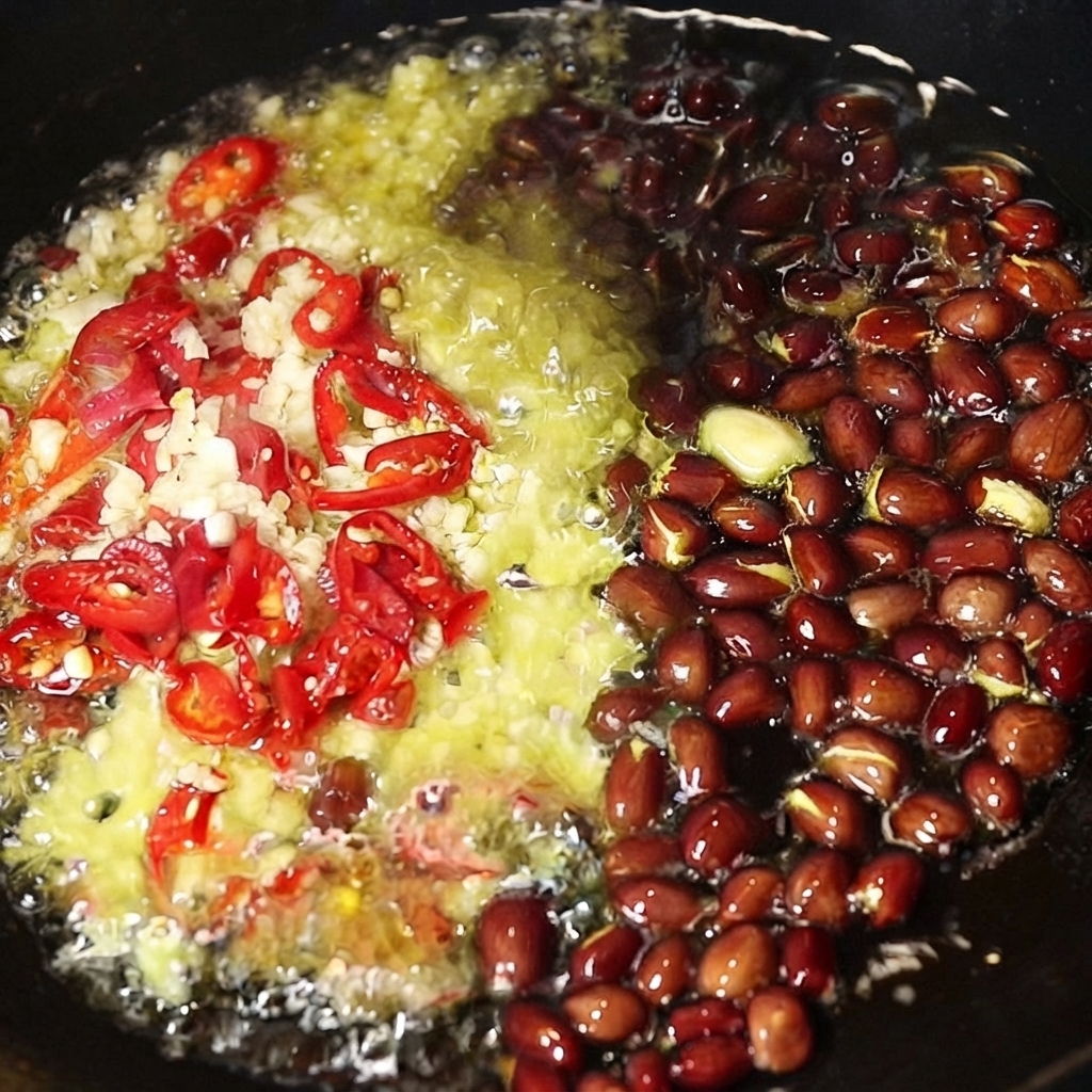 Aglio tritato, peperoncini rossi affettati e arachidi intere che sfrigolano nellolio caldo allinterno di un wok.