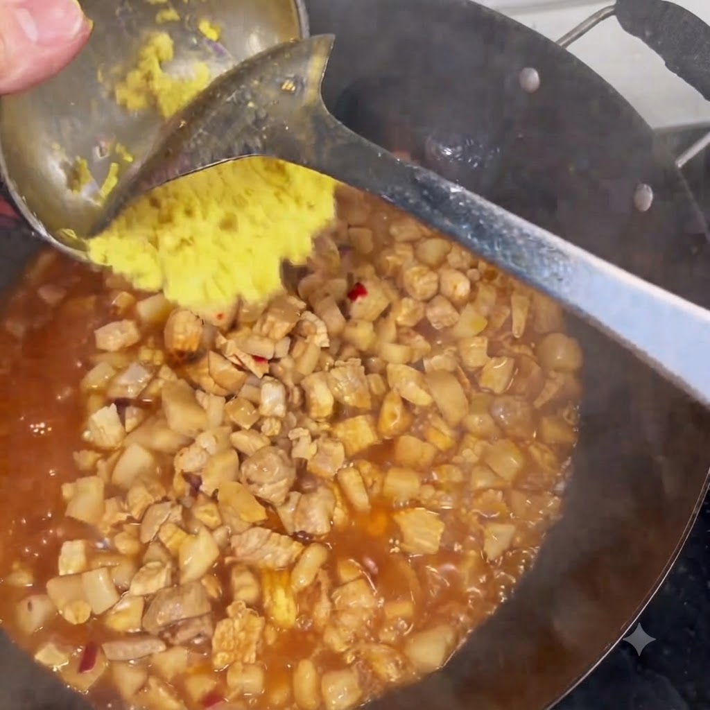 Zenzero tritato raschiato da un mestolo in un wok pieno di carne e salsa in ebollizione.