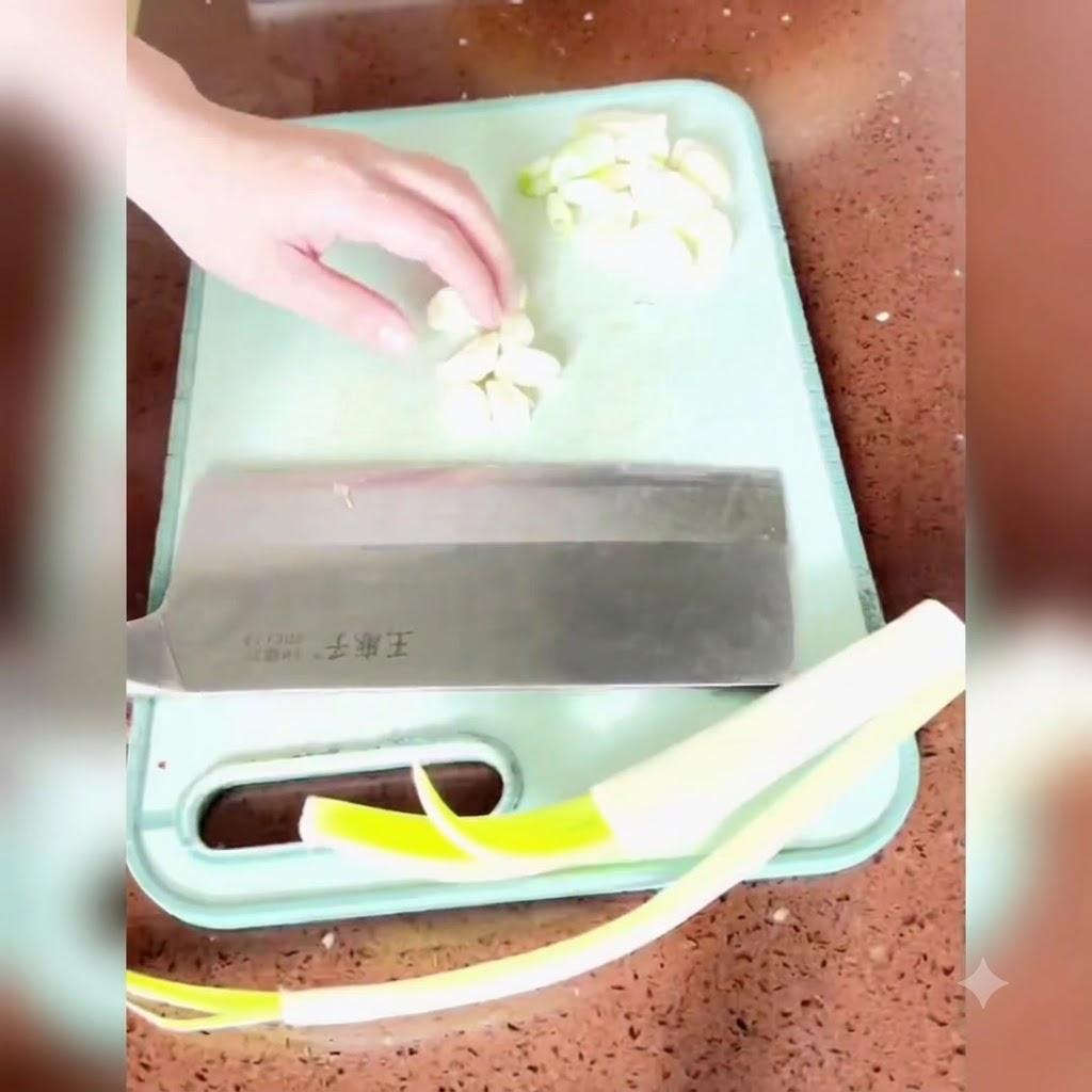 Cipollotti, zenzero e aglio tagliati e tritati finemente su un tagliere verde con una mannaia grande.