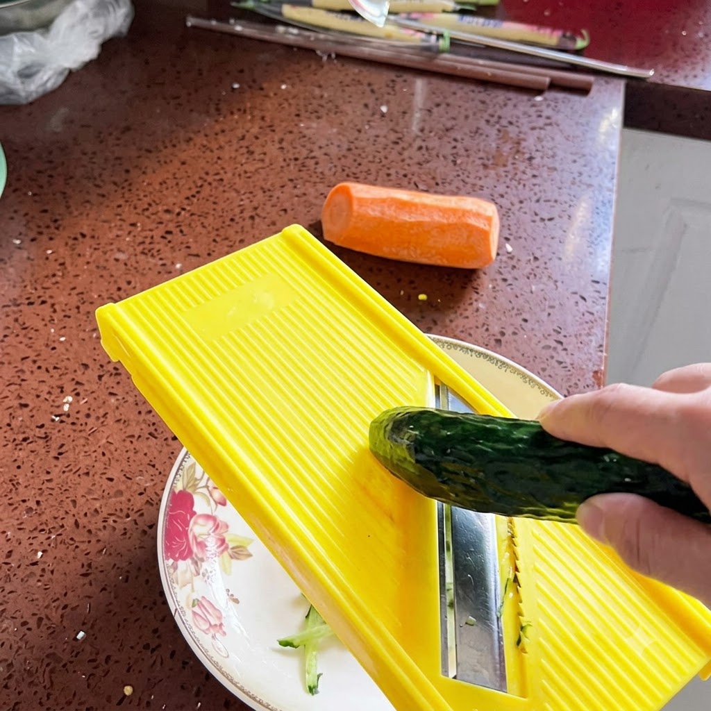 Un cetriolo fresco grattugiato in sottili strisce usando una mandolina giallo vivo sopra un piatto decorativo.