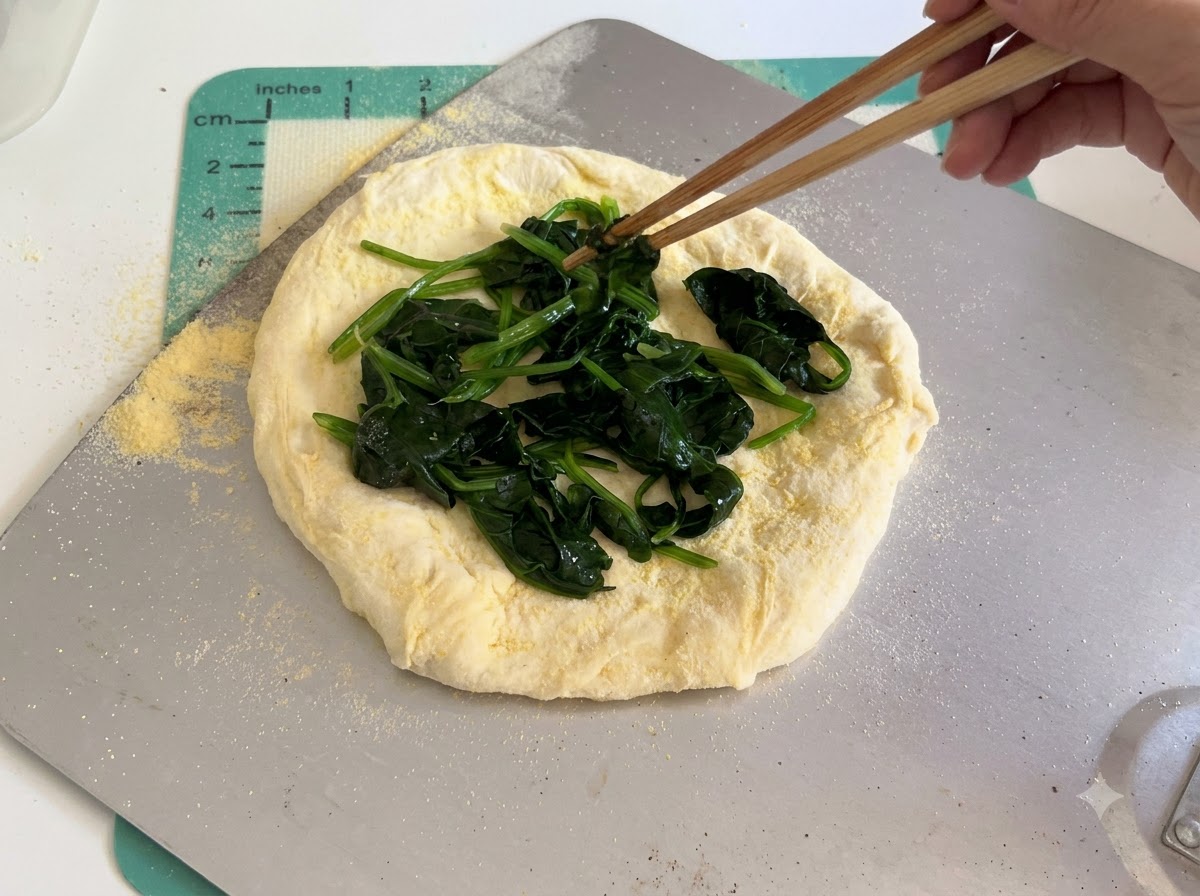 Fette di formaggio bianco disposte con cura sullo strato di spinaci sopra limpasto crudo della pizza usando le bacchette.