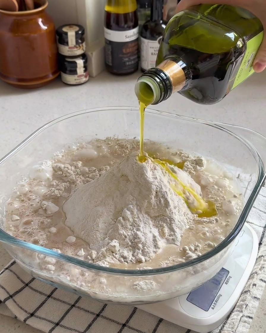 Olio doliva versato su un mucchio di farina e acqua allinterno di una ciotola di vetro trasparente su una bilancia da cucina.