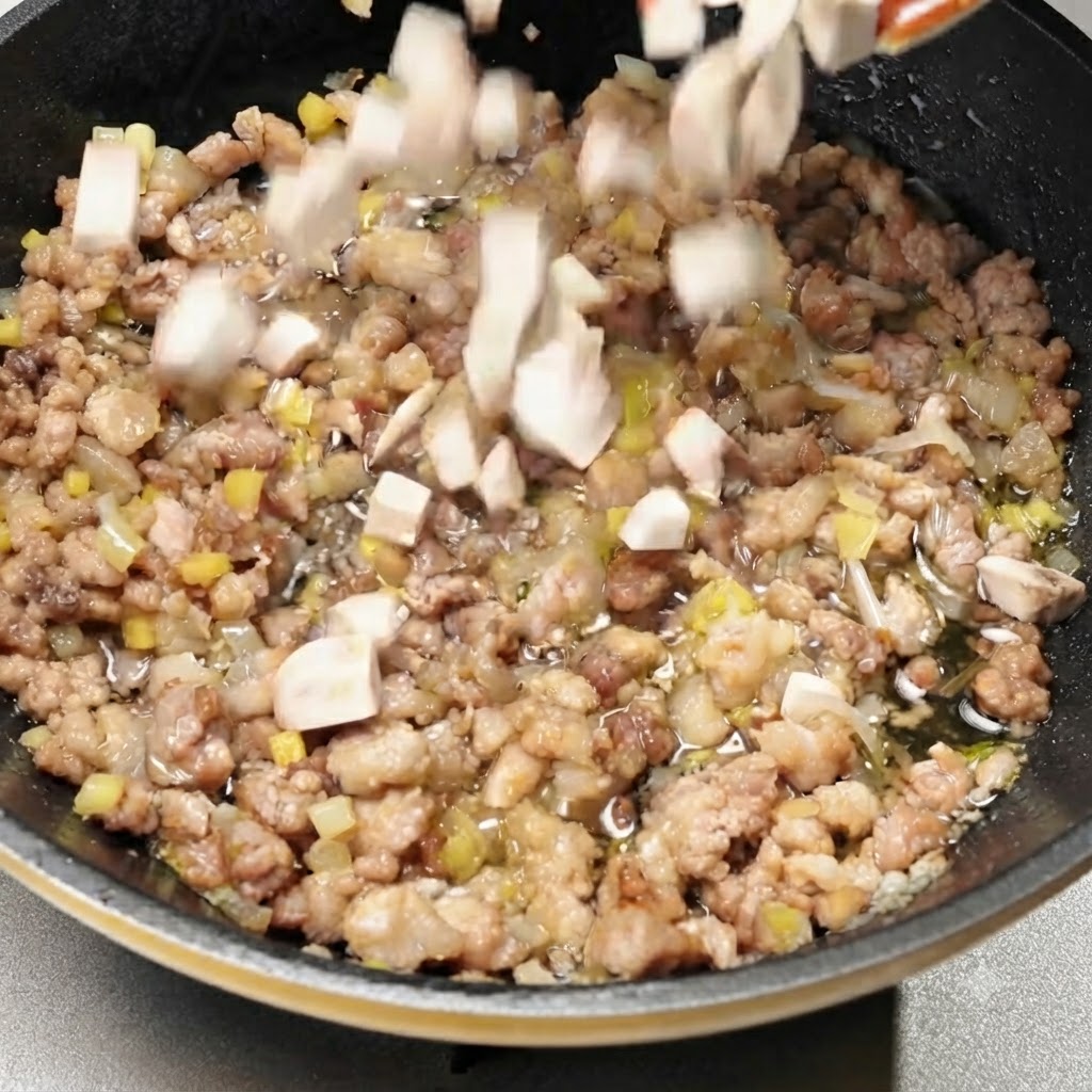 Funghi a cubetti mescolati nella padella con la carne di maiale condita.