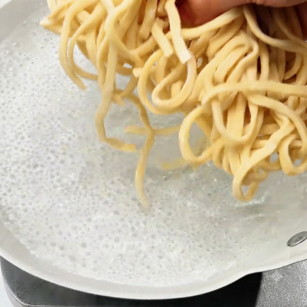 Noodles freschi calati in una pentola di acqua bollente.