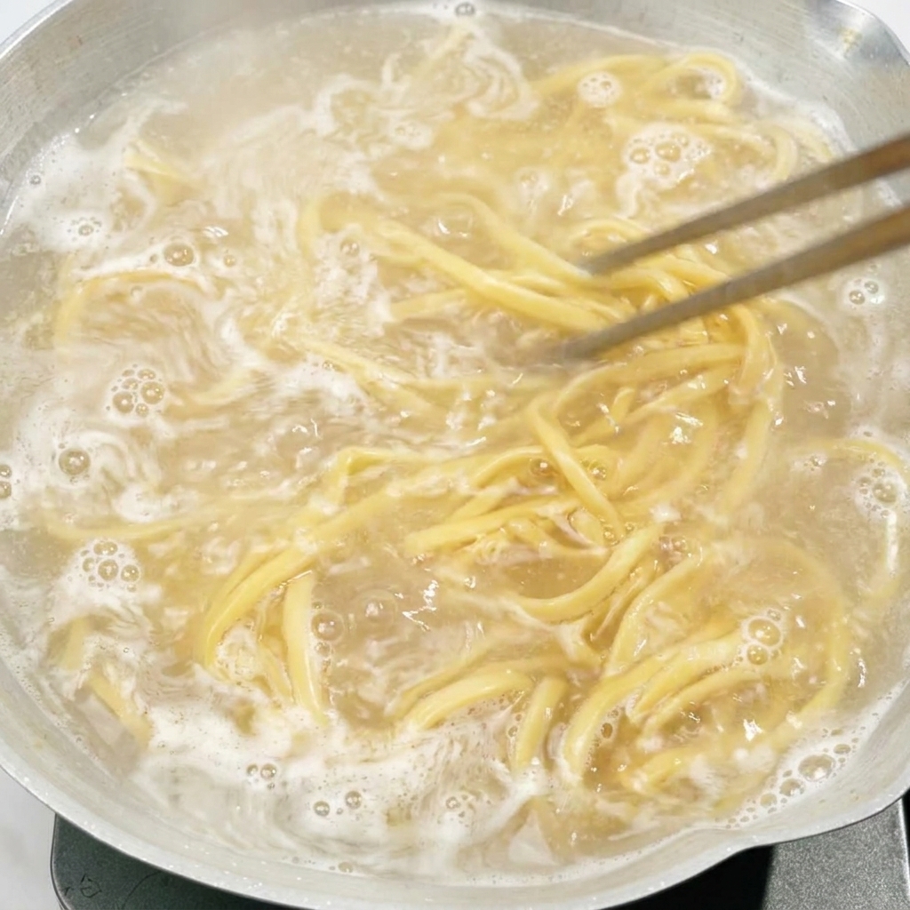Bacchette che mescolano i noodles in ebollizione in una pentola dacqua.