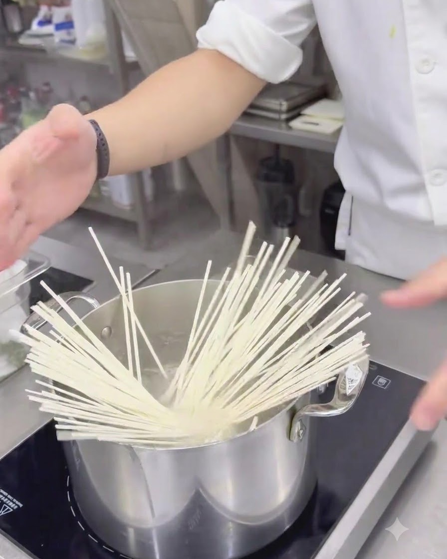 Udon bianchi secchi immersi in una pentola dacciaio inossidabile con acqua bollente.