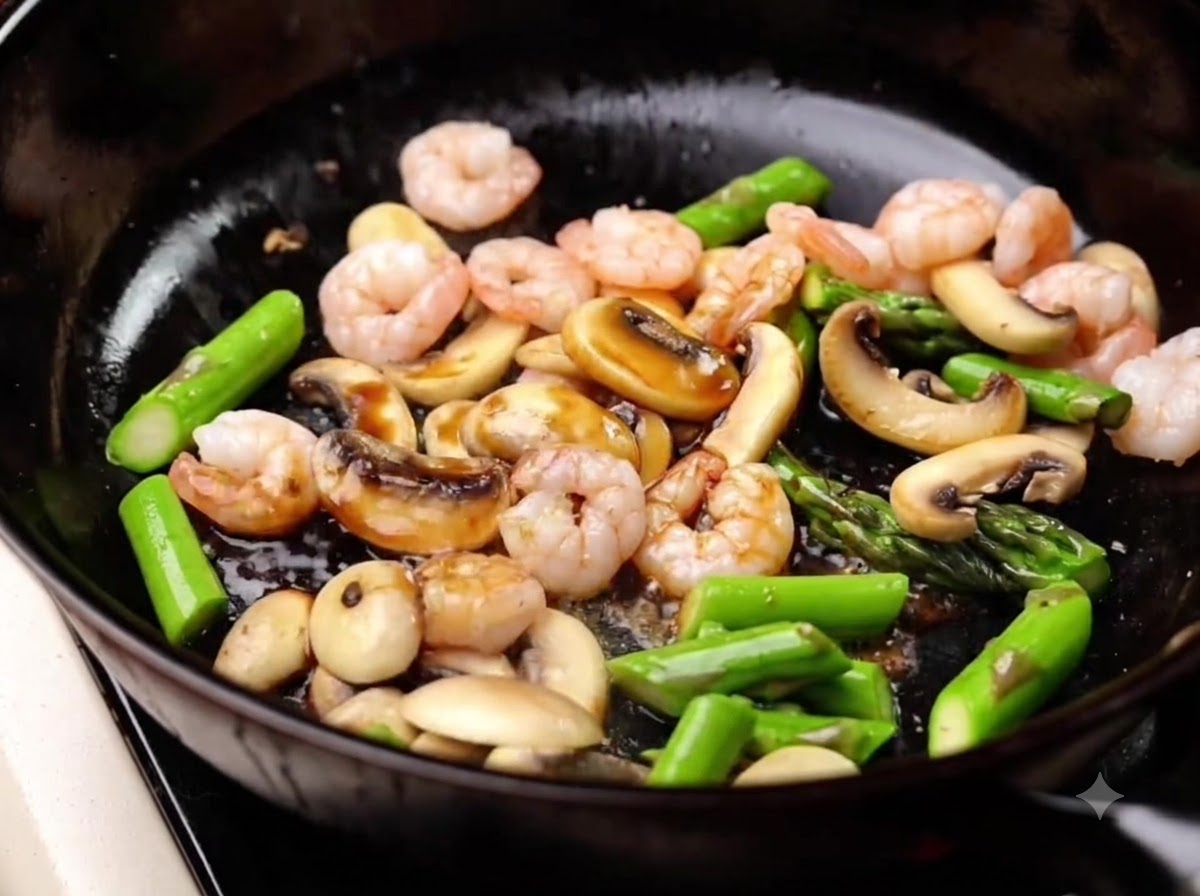 Salsa di soia leggera versata nella padella sopra i gamberi, gli asparagi e i funghi, e mescolata insieme.