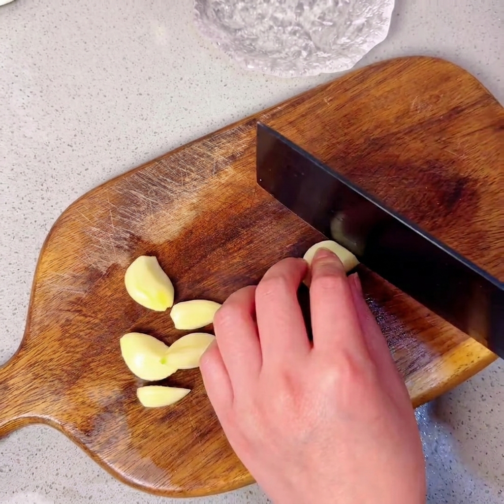 Spicchi daglio disposti su un tagliere di legno pronti per essere triturati.