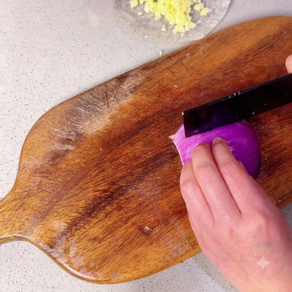 Metà di una cipolla rossa tagliata a piccoli pezzi su un tagliere di legno.