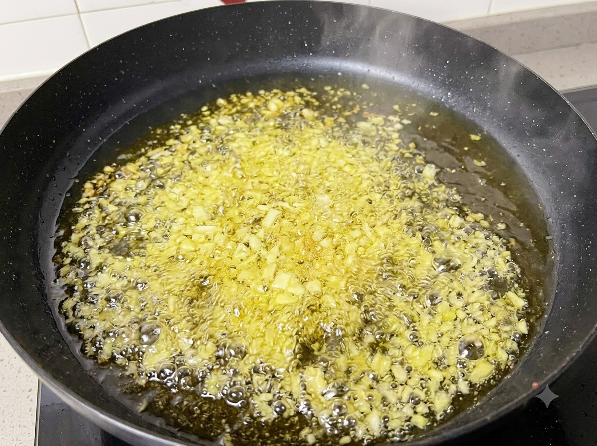 Aglio tritato e cipolle che friggono e fanno le bollicine nellolio caldo dentro una padella nera.