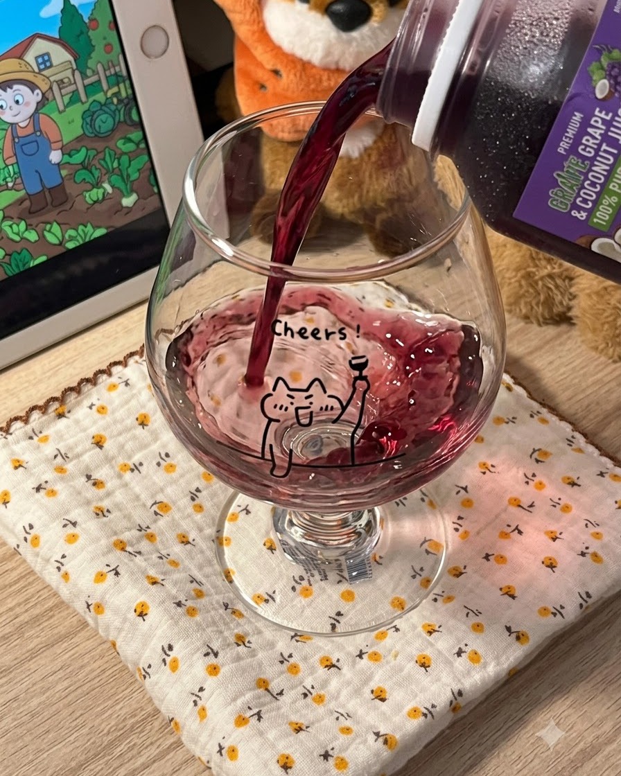 Succo duva viola scuro versato da un cartone in un bicchiere trasparente con stelo decorato con il disegno di un gatto.