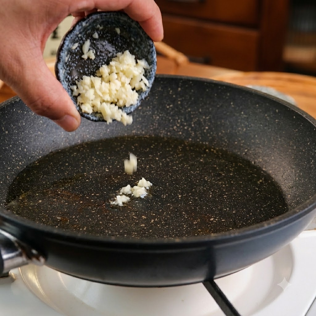 Aglio tritato versato da una ciotolina scura in una padella con olio.