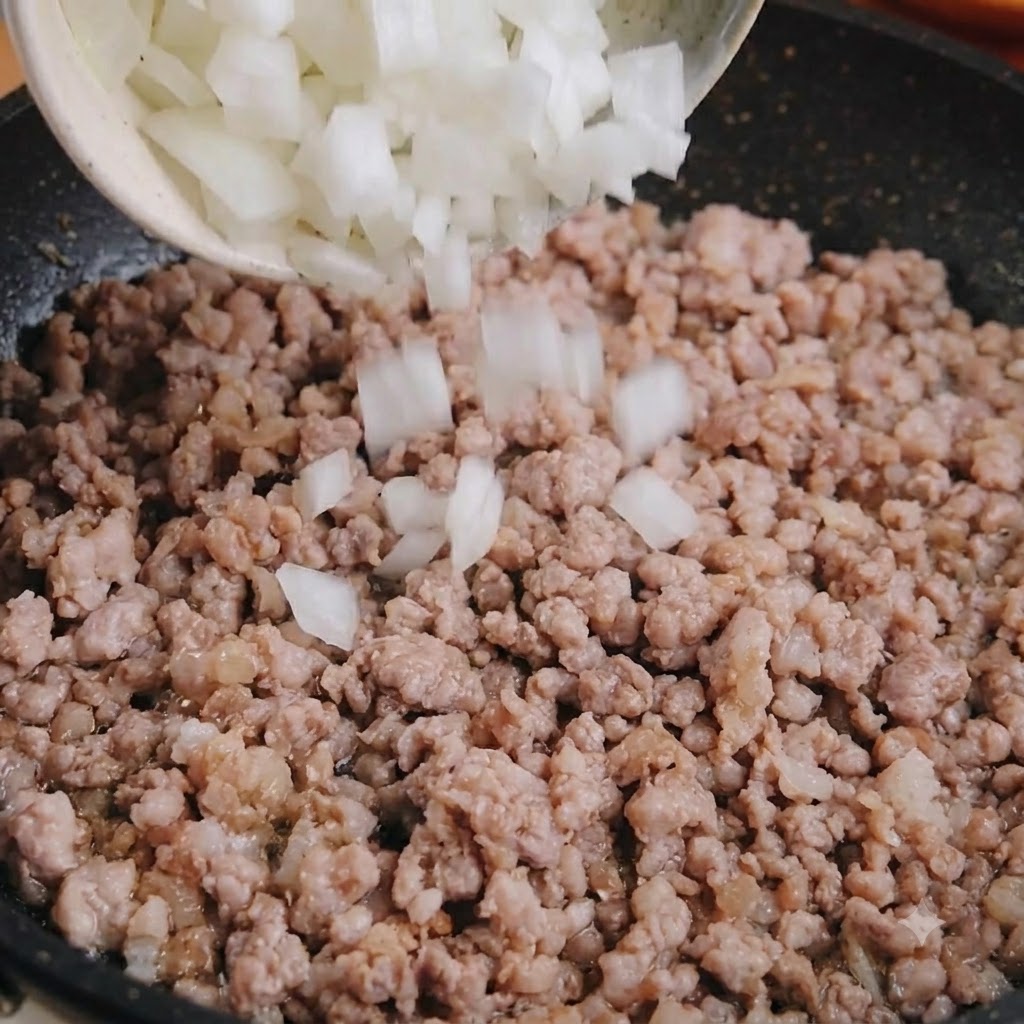 Cipolla bianca a dadini versata da una ciotola in una padella di maiale macinato cotto.