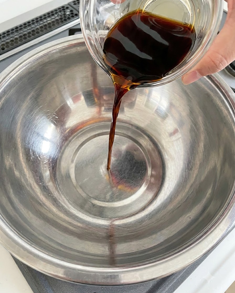 Salsa di soia scura versata da un contenitore di vetro in una ciotola di acciaio inossidabile.
