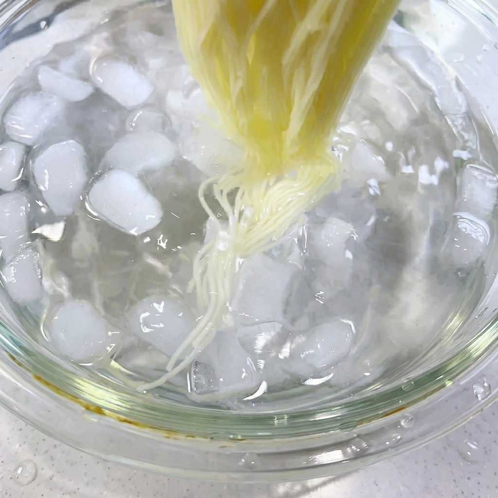 Bacchette che mescolano i noodles cotti in un bagno di acqua e ghiaccio pieno di cubetti di ghiaccio.
