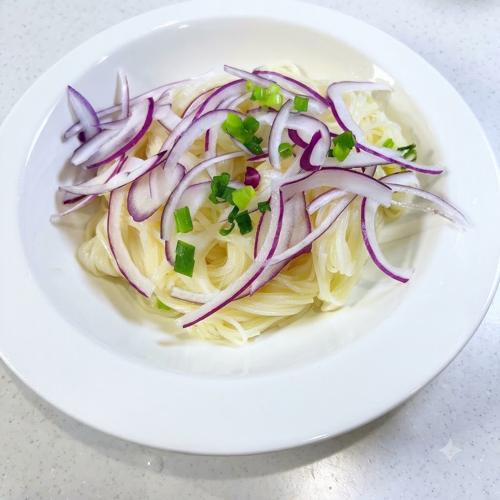 Cipollotti freschi tritati sparsi sui noodles e sulle fette di cipolla rossa in una ciotola bianca.
